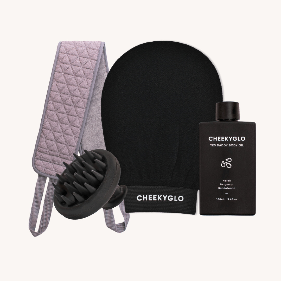 The Everyday Essentials Set by CheekyGlo includes an Exfoliating Body Glove, a scalp scrubber massage brush, a quilted grey back strap with an Exfoliating Back Scrubber feature, and a bottle of "Yes Daddy Body Oil.